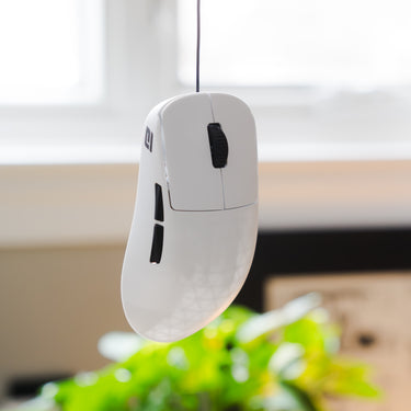 White computer mouse with black buttons hanging by a thin cable against a blurred indoor background